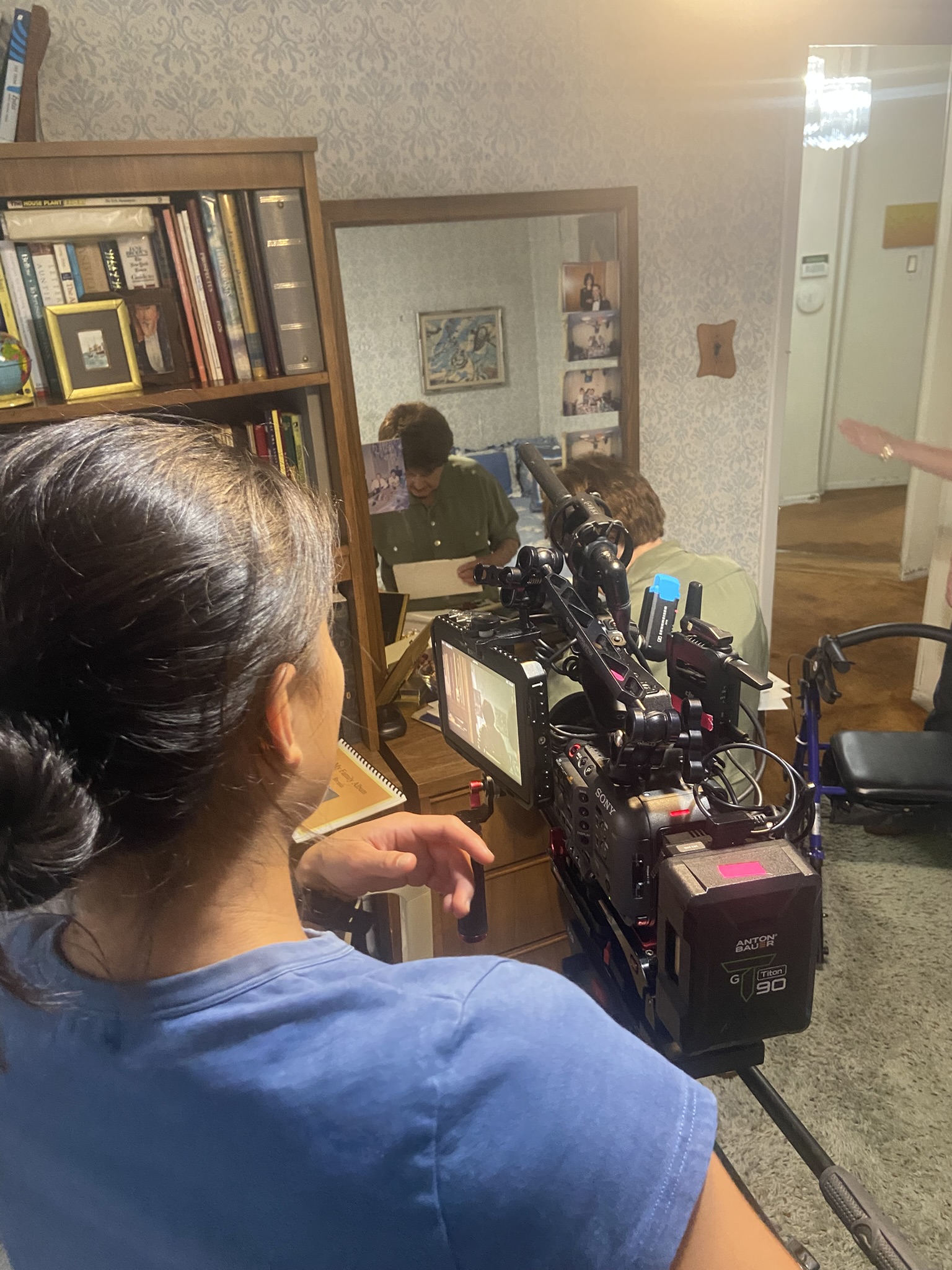 A camera operator frames Bronia and Isaac reflected in a mirror as they look through papers.